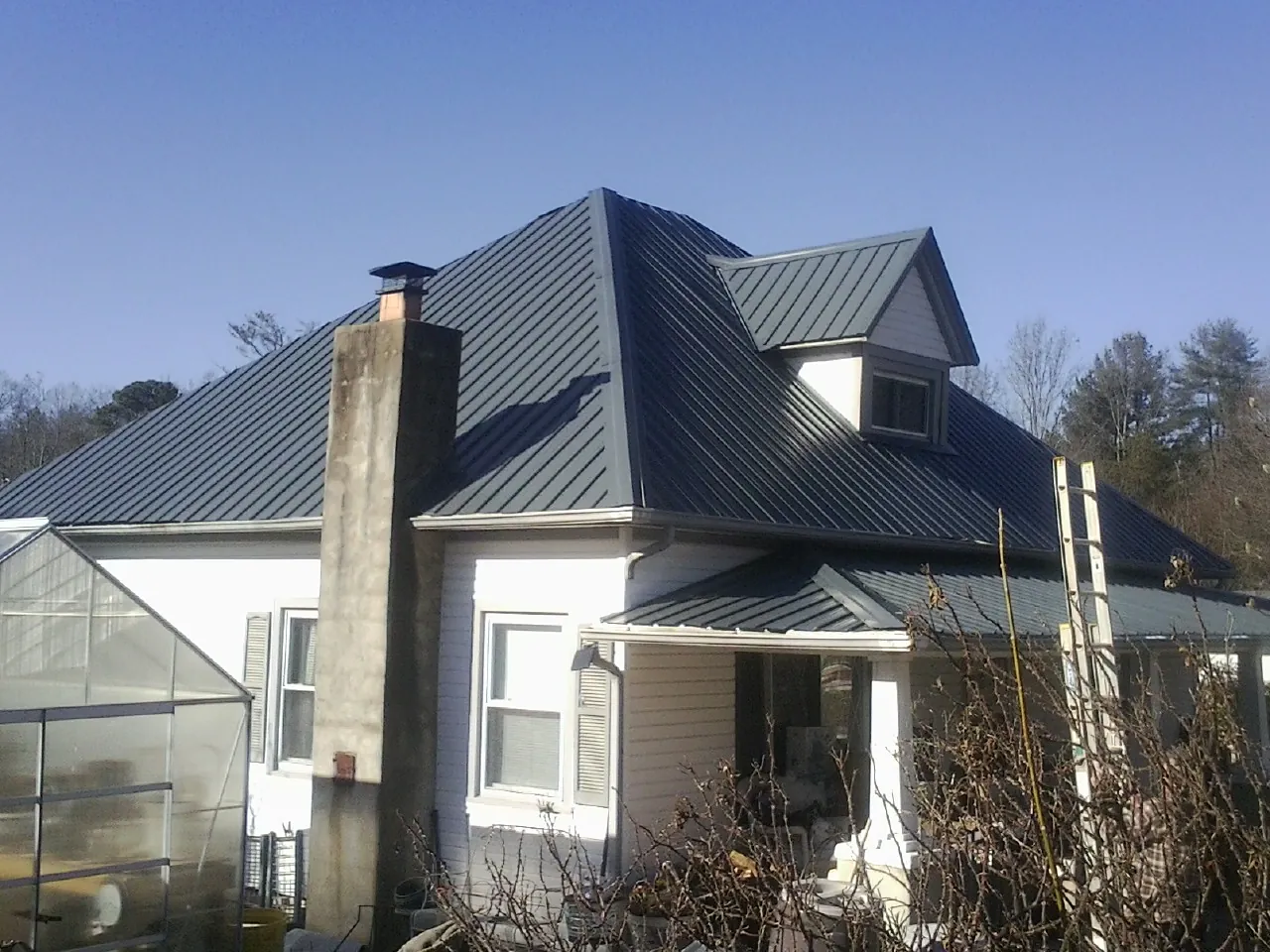 Dark blue standing seam metal roof on a white farmhouse with dormer — Slate & Tile Roof Repair by Roofing Brothers in Dora