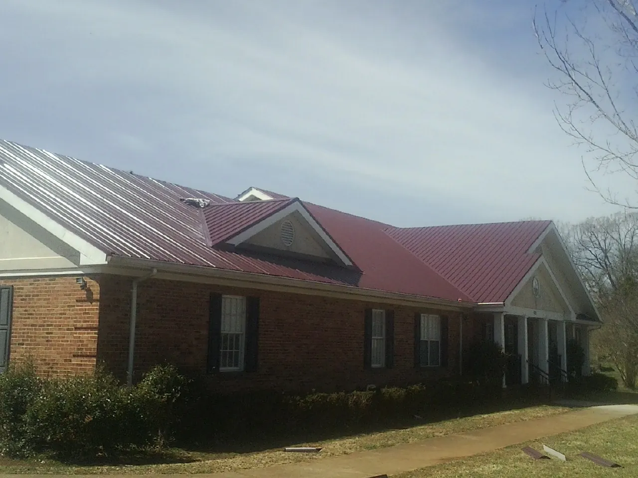 Red metal roof with gabled entries on a long brick building, from a Hail Damage Roof Repair job in Dora