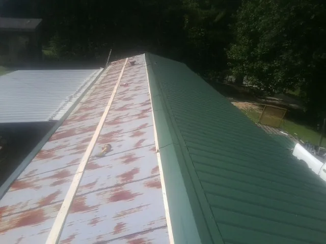 Old rusted panels beside newly installed green metal roofing — Wind Damage Roof Repair by Roofing Brothers in Dora