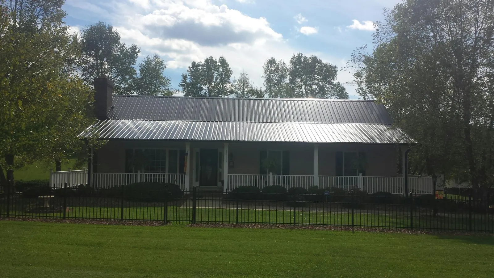 Gray metal roof on a brick ranch with a full width front porch — Gutter Guard Installation work by our crew in Dora