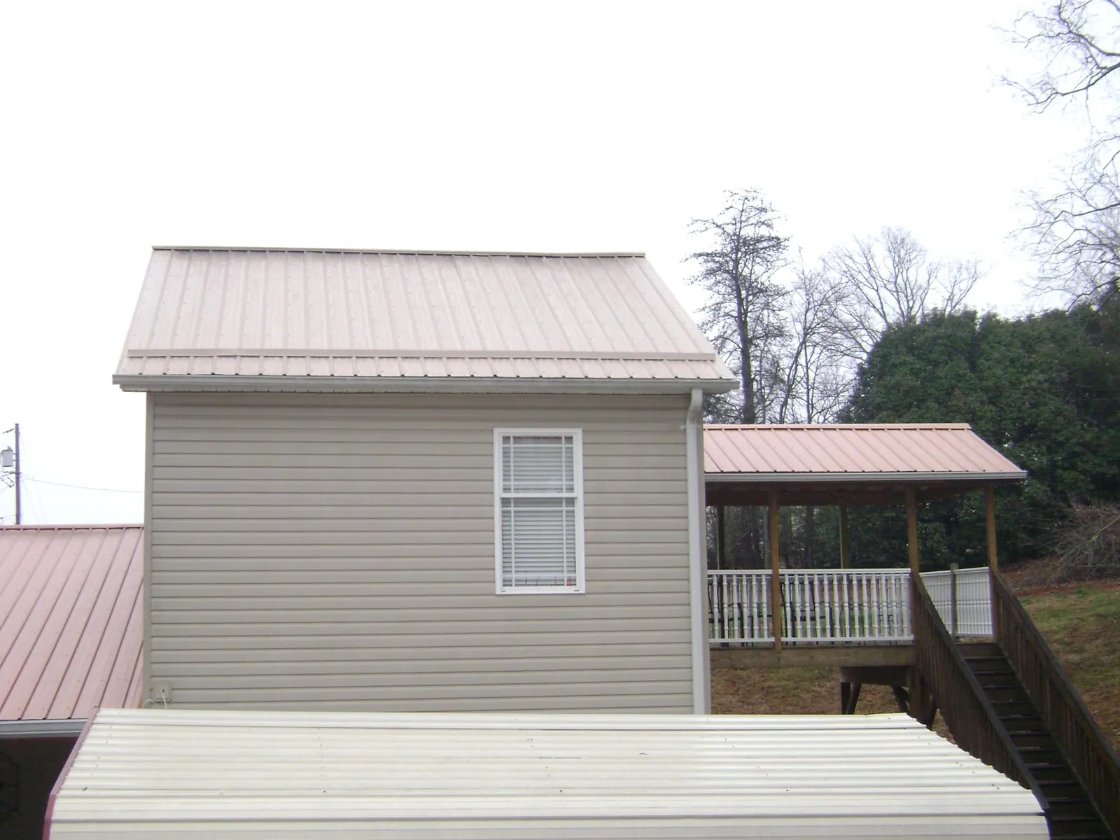 Tan metal roofs on a two story addition and attached porch, from a Roof Replacement job in Dora